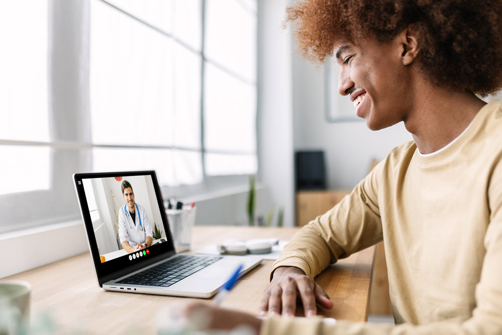 Smiling young man using telehealth to talk with a doctor